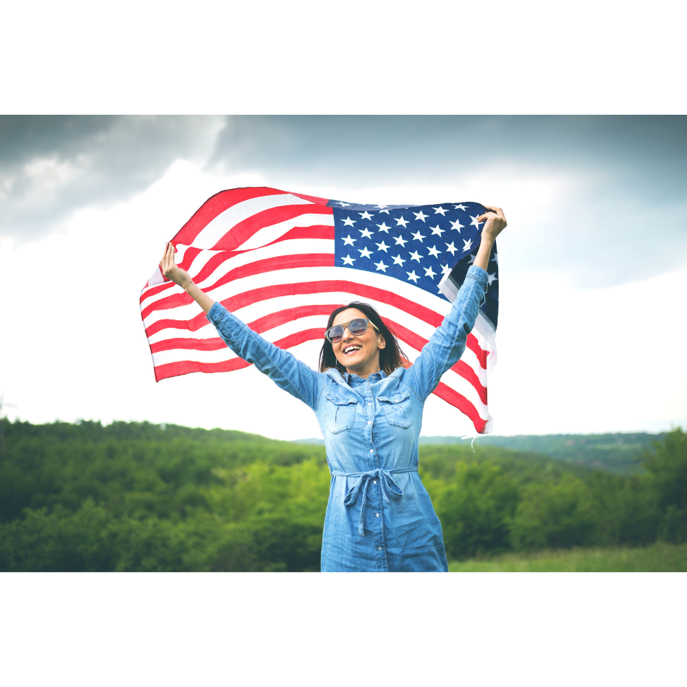 Woman wearing sunglasses, smiling and waving a huge American flag overhead.